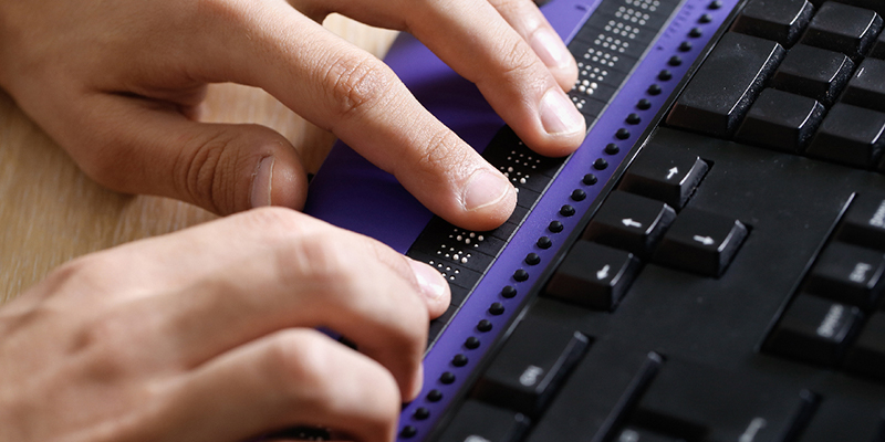 A visually disabled individual using a braille keyboard to look at a webpage.