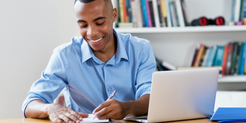 Young black man sitting at desk writing on his paper.
