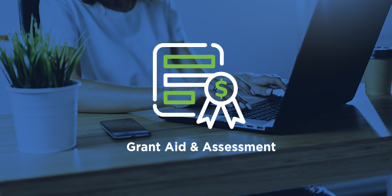 The words "Grant Aid & Assessment" are in front of an administrator working on their laptop.