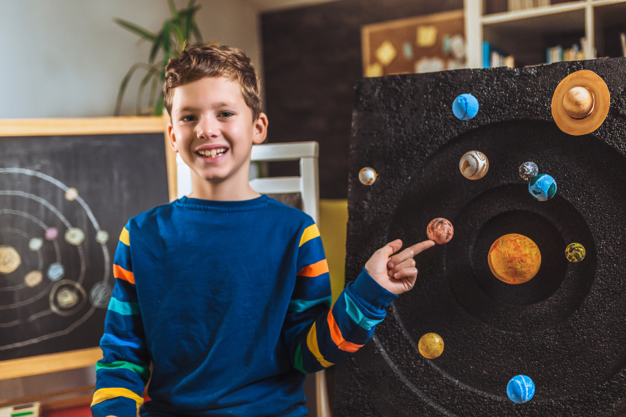 student sitting proudly in front of his solar system presentation