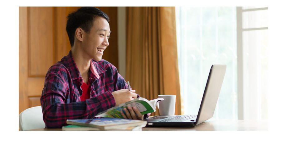 Young man smiling while looking at laptop and taking notes.