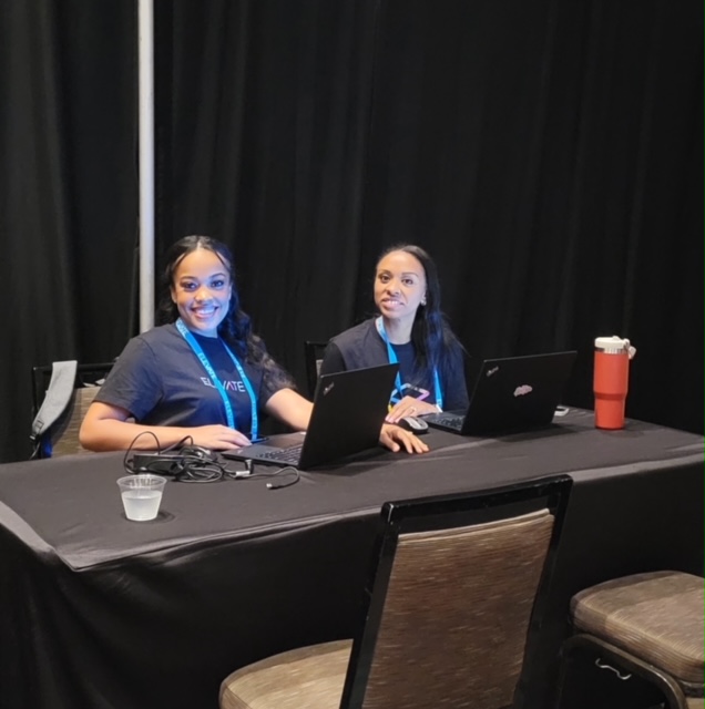 Two smiling Elevate 2023 attendees using their laptop computers