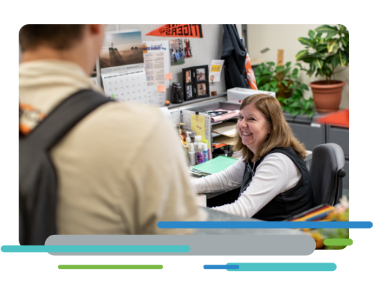 Administrative office worker at a desk, smiling at a student