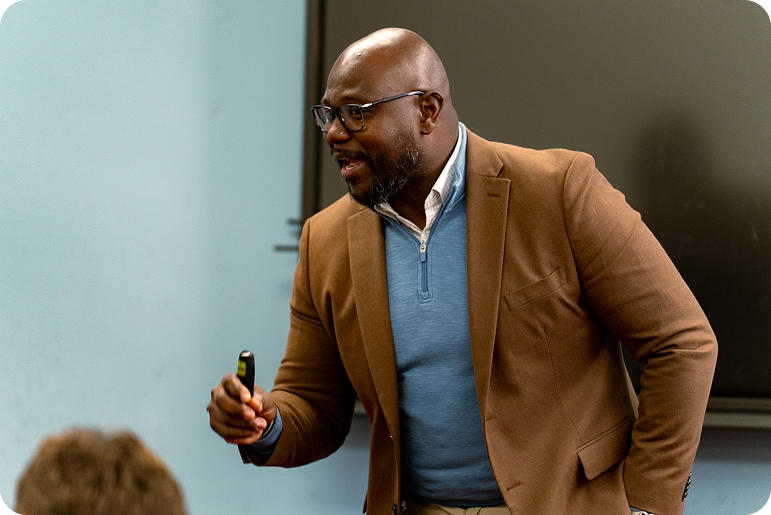 Instructor speaks to a group while holding a marker or remote in a classroom