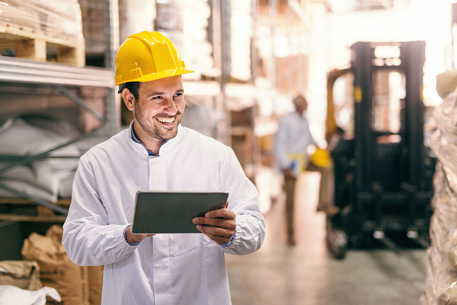 Smiling warehouse employee in a hard hat using a tablet device