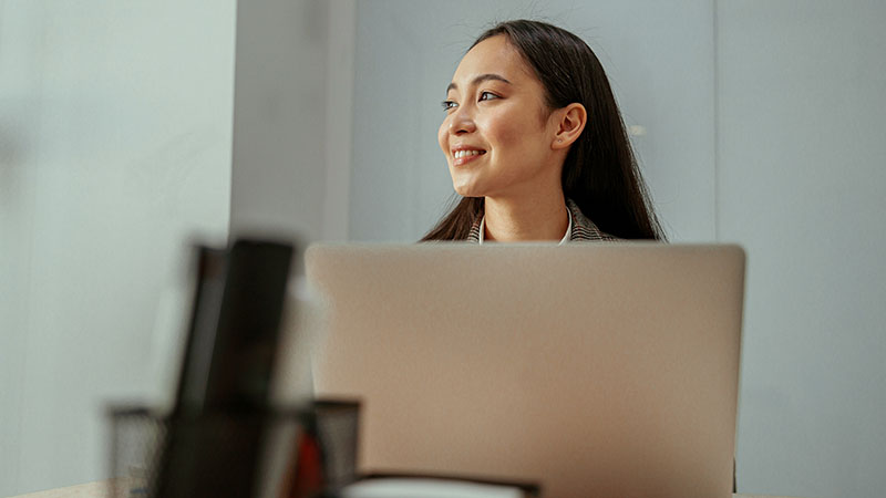 Charming Asian woman working at the office using a laptop looking away.